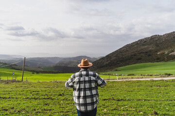 Chico grande con camisa y sombrero frente a paisaje montañoso levantando los brazos y agarrando sombrero en señal de libertad