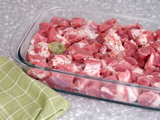 Sliced pieces of pork with a single bay leaf on them in a glass baking tray