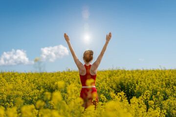back view of a young woman wearing red with arms raised in a yellow field