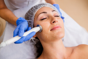 Gorgeous woman with smooth skin getting cosmetology procedures in modern beauty salon. Hands of...