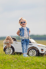 girl in sunglasses stands in front of a white children's car