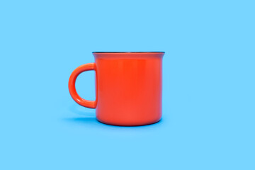 Orange mug on a blue background with free space for text. Orange cup with a drink on a blue background. Cafe or snack concept. Orange mug with the possibility of applying advertising or logo