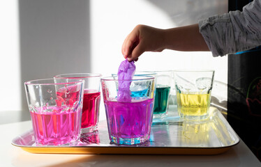 Artistic education and fun of little child. Hand of kid with dye making colorful water in glasses. Positive activity with color for autistic child. Kindergarten and play. Closeup.