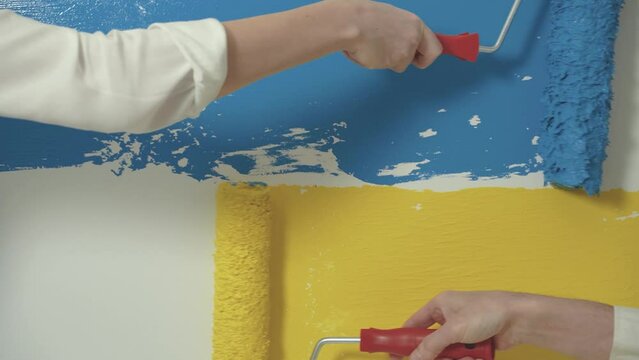 Flag of Ukraine grunge style banner background. Hands hold brush roller and paint the wall. Blue yellow Ukraine flag banner concept. No war. Peace. Faceless.