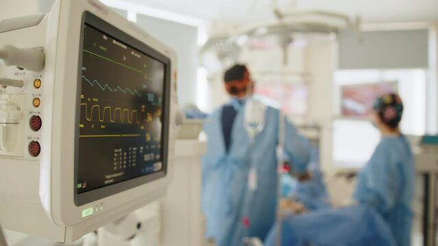 Heart monitor in hospital operating theatre. Heart rate and patient control monitor in hospital theater room during operation. Medical Team Performing Surgical Operation in Modern Operating Room.