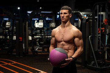 Fototapeta na wymiar Muscular man with fit torso holding medicine ball in gym, workout