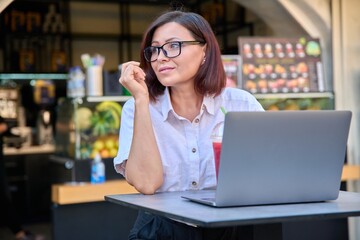 Middle-aged woman with laptop at table in an outdoor fruit juice bar with fresh juice