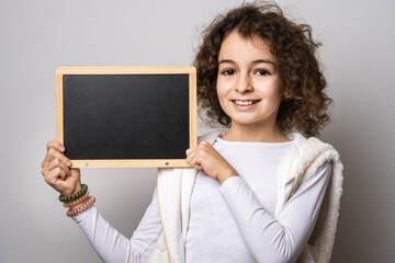 One small caucasian girl ten years old with curly hair front view portrait close up standing in front of white background looking to the camera hold board for text copy space