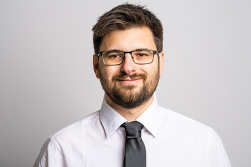 Portrait of one adult caucasian man 30 years old with beard and eyeglasses businessman or doctor looking to the camera in front of white wall background wearing shirt confidence success concept