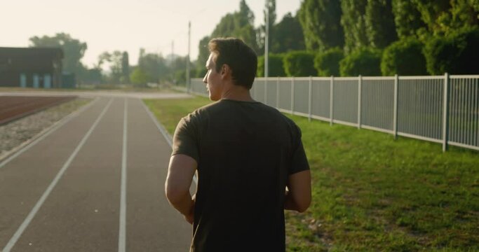 Rear view of sport man running outdoors. Portrait of running man jogging at stadium. Sport workout outdoor at sunset. Athletic training run exercise