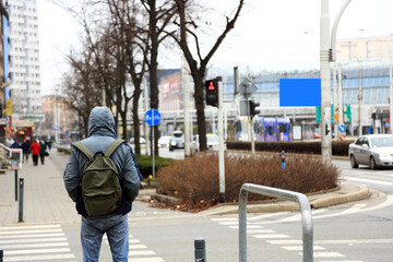 Młody mężczyzna z plecakiem stoi przed przejściem dla pieszych we Wrocławiu.	