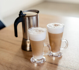 Two latte macchiato coffee in the glass with milk foam on wooden table, moka pot, home made.
