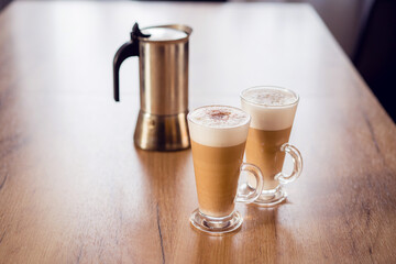 Two latte macchiato coffee in the glass with milk foam on wooden table, moka pot, home made.
