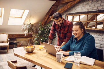 Young happy students cooperating while learning on laptop at home.