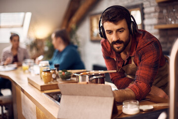 Young man uses digital tablet while preparing lunch at home.