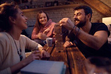 Young happy friends play jenga tower game in the evening at home.