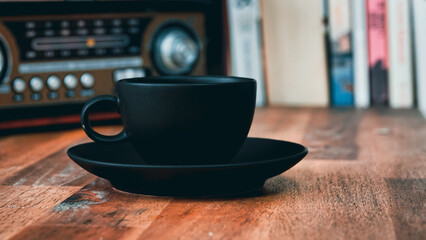  vintage radio, a black coffee cup and saucer on a brown wooden table, with books in the background, vintage look	