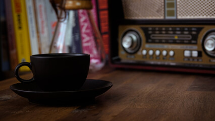 coffee brewing jug, vintage radio, a black coffee cup and saucer on a brown wooden table, with books in the background, vintage look	