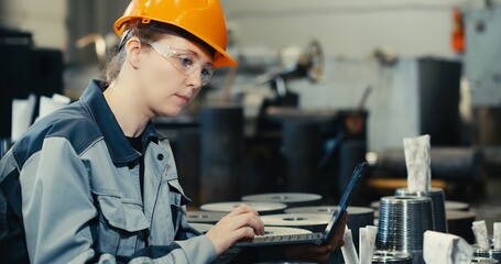 Oil refinery plant engineer in work uniform using laptop computer with spreadsheet software. Work with software at an oil-producing industrial enterprise intended for the production of parts.