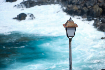 Old lantern at the volcanic shore of El Hierro with a wavy ocean in the background. Electricity on...