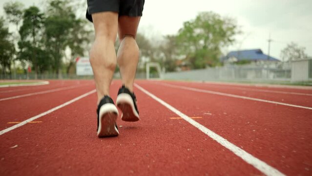 Close up legs Young chinese man wearing sportswear running on track at sport stadium. Fit man jogging outdoor cross the finish line. Exercise in the morning. Healthy and active lifestyle concept.