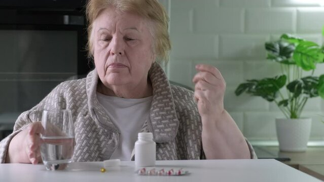 Senior woman takes tablet and drinking a glass of water at home. Single retired female indoors. Old age, health care, retirement and people concept