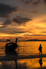 Silhouettes of a boat and a young woman on the beach at sunset