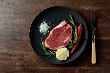 Raw beef steak with rosemary, garlic, salt, and pepper.