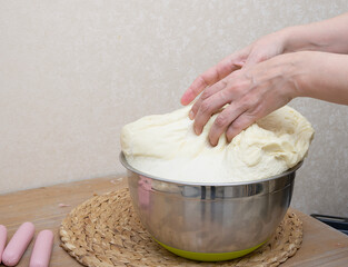 Women's hands carefully knead the dough in a large pot in the home kitchen for making hot dogs - close-up of women's hands. Mastery of cooking at home.