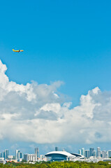 front view, very far distance of a commercial, passenger jet flying over skyline of Miami, Florida at midmorning