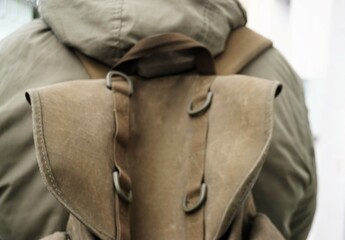Rücken von jungem Mann mit grüner Kapuzenjacke und Militärrucksack 