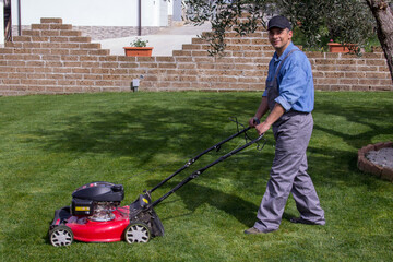 Smiling handyman man while cutting the grass at the lawn. Gardening work