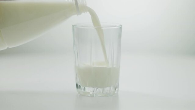 Close-up transparent glass with white milk pouring from bottle. Fresh calcium dairy product filling drinking glass indoors on table. Healthy eating concept