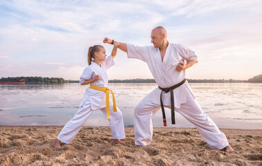 Sensei and her young female student are training on the sand, against the backdrop of the river and the sky at sunset © VlaDee