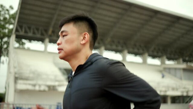 Attractive Young chinese man wearing sportswear running on track at sport stadium. Fit man jogging outdoor cross the finish line. Exercise in the morning. Healthy and active lifestyle concept.