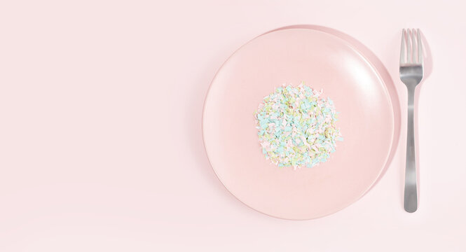 A plate full of microplastics on a pink background. Impact of micro plastic in food chain. The concept of plastic pollution. Composition of plate, fork and micro plastic. Copy space