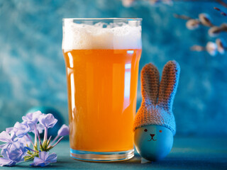 A glass of craft beer for Easter. Crocheted hat with bunny ears on an Easter egg. Funny face, blue...