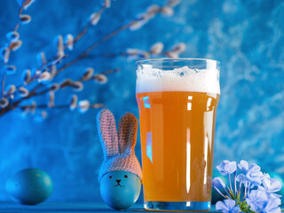 A glass of craft beer for Easter. Crocheted hat with bunny ears on an Easter egg. Funny face, blue...