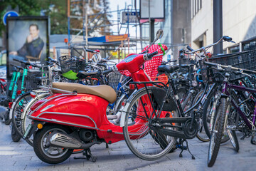 Fototapeta na wymiar Vivid red scooter standing near many different bicycles on parking