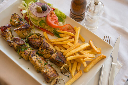 Bandeja con brochetas de carne, patatas fritas y ensalada