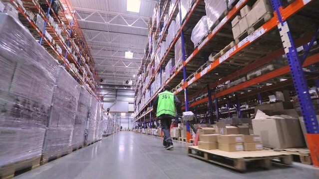 A man in a warehouse is carrying a rokla. A man in a large warehouse is carrying a rokla. Warehouse worker. Large modern warehouse
