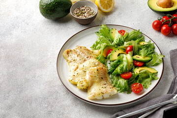 Fried cod fillet with salad, green leaves, avocado, seeds, tomatoes cherry. Grey background.