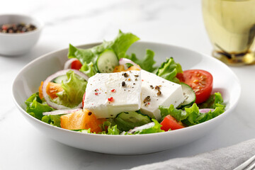 Delicious greek salad with vegetable and feta cheese, close up. Pepper and bottle of oil. Marble background.
