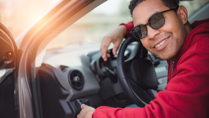 Fototapeta na wymiar handsome Hispanic young man who sits in car and uses cell phone