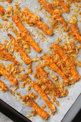 Roasted carrot sticks with cheese and garlic. In a dark square baking tray with paper. Top view. Healthy snacks, vegetarian