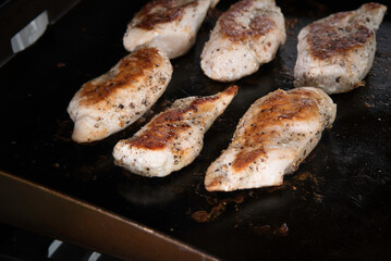 Marinated chicken breast cooking on an outdoor griddle with steam rising.