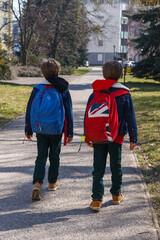 Two children walking with backpacks to school along an alley housing estate - obrazy, fototapety, plakaty