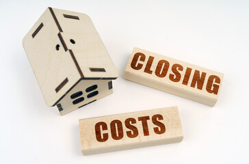 On a white surface, a wooden toy house and blocks with the inscription - CLOSING COSTS