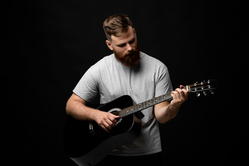 Handsome brunette bearded guitarist plays an acoustic guitar in a black room. The concept of music...