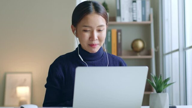 Young Asian woman creator talking on video call conference or virtual meeting at home via laptop